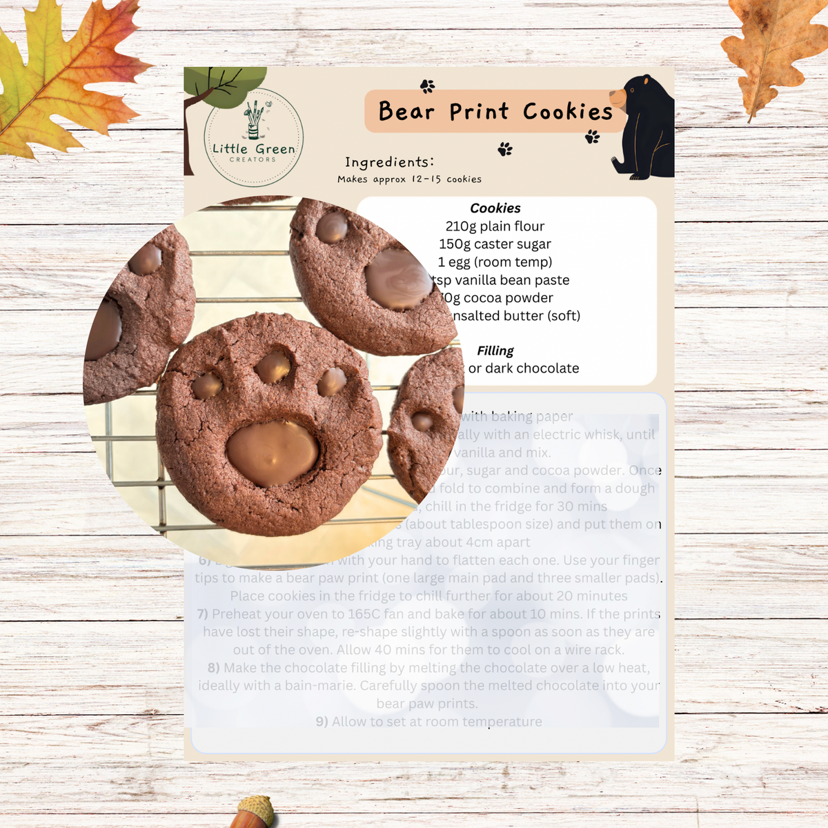 A recipe card for 'Bear Print Cookies' from Little Green Bakes, displayed on a whitewashed wood background with autumn leaves. The card details the ingredients and instructions for making chocolate chip cookies, with two baked cookies shown on the left.