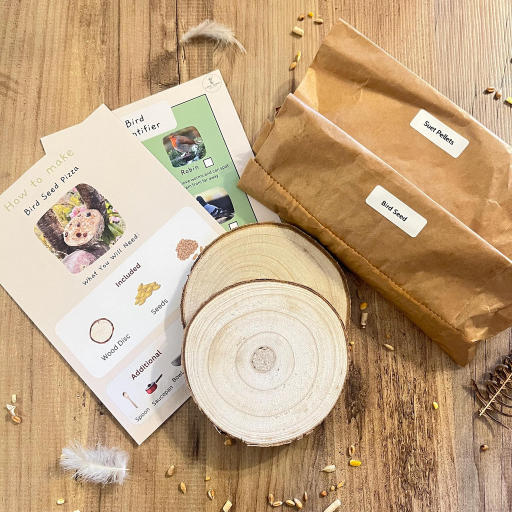 Bird seed making kit with wooden discs, instructions, and brown paper bag on a wooden surface labelled with bird seed and suet pellets.